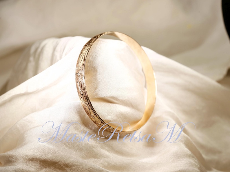 May include: A gold bangle bracelet with an intricate floral design. The bracelet is smooth and shiny.