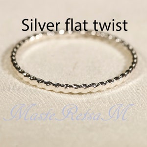 May include: A silver flat twist ring. The ring has a textured, rope-like design around the band. The text "Silver flat twist" is above the ring. The ring is on a light-colored surface.