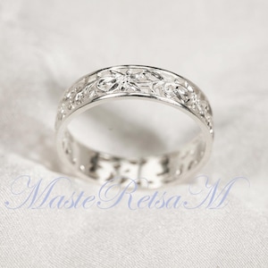 May include: A silver ring with a floral filigree design. The ring has an openwork pattern of flowers and leaves around the band. The ring is displayed on a white surface.