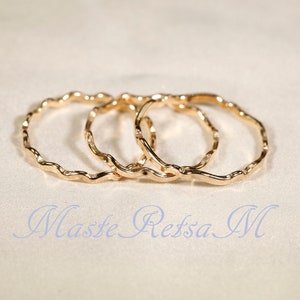 Puede incluir: Tres anillos de color dorado con un diseño ondulado y texturado. Los anillos están apilados uno encima del otro.