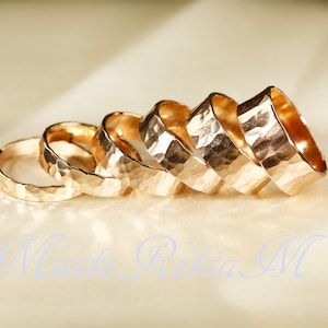 May include: Five gold hammered rings stacked on top of each other. The rings are all different sizes and have a textured surface.