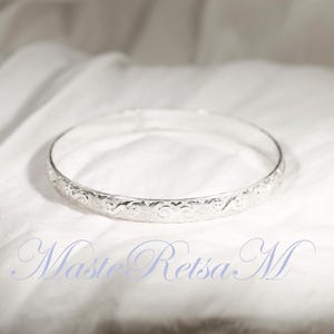 May include: A silver bangle bracelet with an intricate floral design.