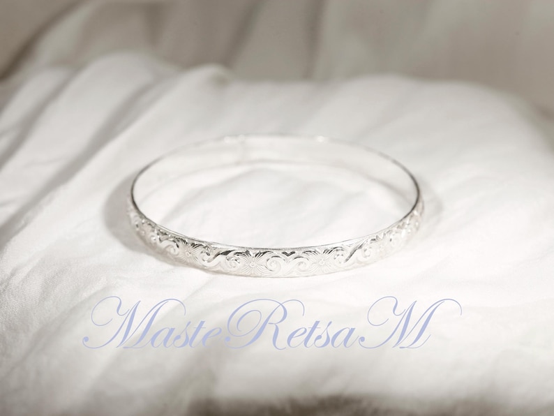 May include: A silver bangle bracelet with an intricate floral design.