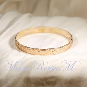 May include: A gold bangle bracelet with a floral design. The bracelet is smooth and shiny.