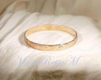 May include: A gold bangle bracelet with a floral design. The bracelet is smooth and shiny.