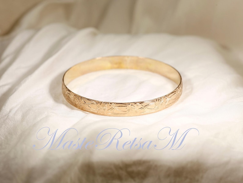 May include: A gold bangle bracelet with a floral design. The bracelet is smooth and shiny.
