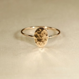 May include: A gold oval ring with a hammered texture. The ring is simple and elegant.