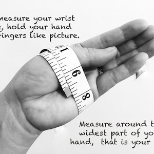 May include: Black and white image showing how to measure your wrist size. A hand is holding a tape measure around the wrist. The text reads: "To measure your wrist size, hold your hand and fingers like picture. Measure around the widest part of your hand, that is your size."
