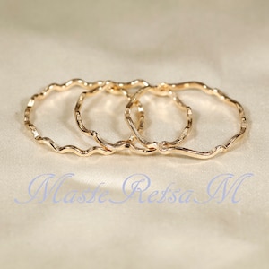 May include: Three gold-toned, wavy, open rings stacked together. The rings are made of thin metal and have a slightly irregular shape.