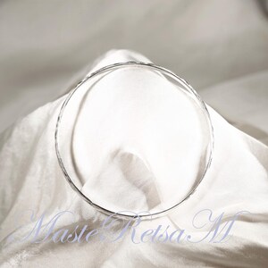 May include: A silver hammered bangle bracelet. The bracelet is round and has a smooth, polished finish.