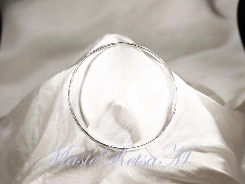 May include: A silver hammered bangle bracelet. The bracelet is round and has a smooth, polished finish.