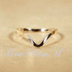 May include: A gold-toned ring with a V-shaped design. The ring is made of hammered metal and has a textured finish.