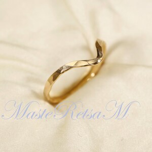 May include: A gold-toned ring with a wavy, textured design. The ring is open and has a slightly pointed end.