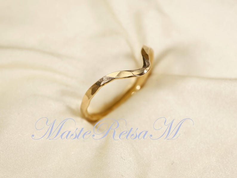 May include: A gold-toned ring with a wavy, textured design. The ring is open and has a slightly pointed end.