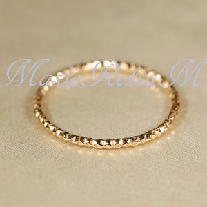 May include: A thin gold band ring with a textured, diamond-shaped pattern.
