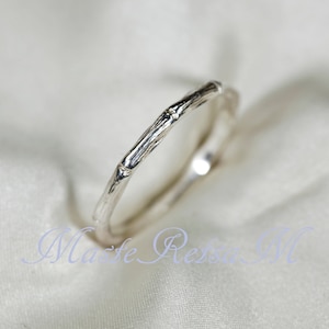 May include: A silver ring featuring a textured band that mimics the appearance of a bamboo stalk with distinct nodes and segments. The metal has a polished finish that reflects light, and the text "Maste Ressa M" is visible in light blue.