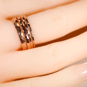 May include: Three hammered rose gold rings stacked on a finger. The rings are a popular style of jewelry.