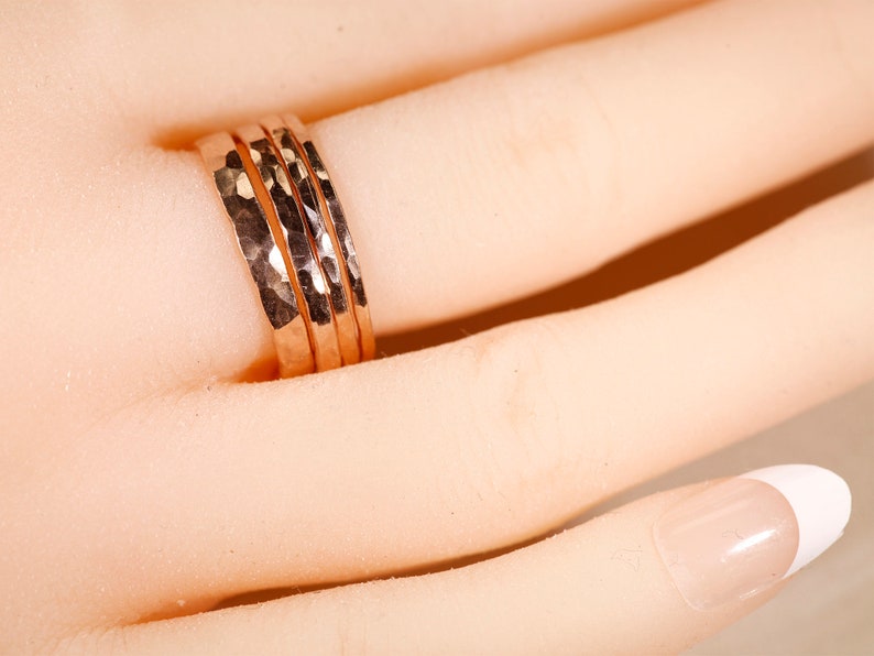 May include: Three hammered rose gold rings stacked on a finger. The rings are a popular style of jewelry.