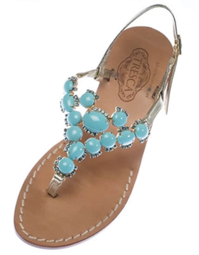 May include: Gold leather sandals with a turquoise gemstone embellishment. The sandals have a strap that goes around the ankle and a toe thong. The brand name "TRESCA" is visible on the insole.