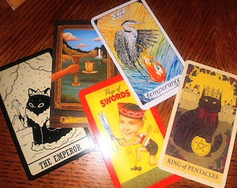 May include: A spread of tarot cards featuring a black cat with a crown, a blue heron, a boy with scissors, and a black cat with a crown and a pentagram.