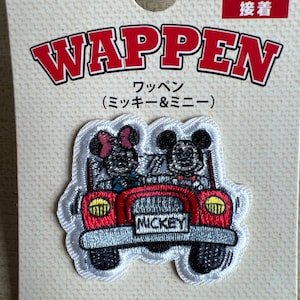 May include: A Disney patch featuring Mickey and Minnie Mouse in a red car. The patch is white with a red car and the word "MICKEY" on the license plate. The packaging includes the word "WAPPEN" in large red letters.