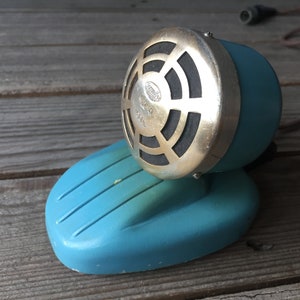 May include: A vintage blue and silver microphone with a round speaker and a cord. The microphone is sitting on a wooden surface.