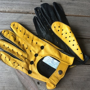 May include: A pair of yellow and black leather driving gloves with perforated detailing. The gloves have a snap closure and a label that reads "Made in Italy".