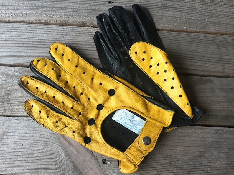 May include: A pair of yellow and black leather driving gloves with perforated detailing. The gloves have a snap closure and a label that reads "Made in Italy".
