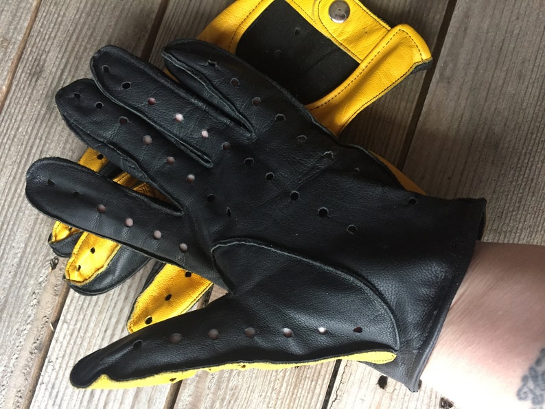 May include: Black leather driving gloves with yellow accents and perforated detailing.