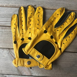 May include: A pair of yellow leather driving gloves with black accents and perforations. The gloves have a snap closure on the wrist.