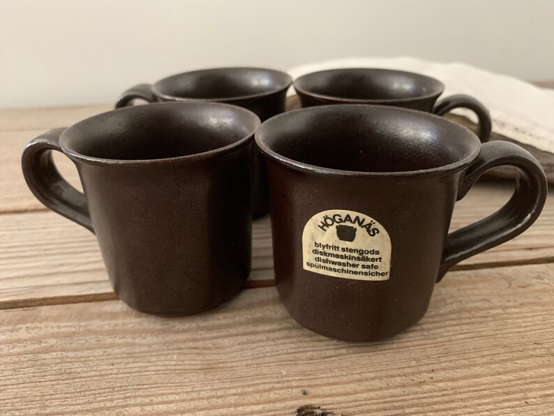 Puede incluir: Cuatro tazas de cer&aacute;mica marr&oacute;n con una etiqueta blanca que dice "H&Ouml;GAN&Auml;S blyfritt stengods diskmaskins&auml;kert dishwasher safe sp&uuml;lmaschinenischer".