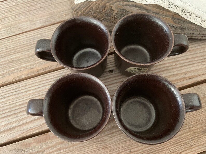 Puede incluir: Cuatro tazas de cer&aacute;mica marrones con un esmalte marr&oacute;n oscuro. Las tazas tienen una forma redondeada y un asa en el lateral.