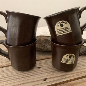 Puede incluir: Cuatro tazas de cer&aacute;mica marr&oacute;n con una etiqueta blanca que dice "Hogan&auml;s Blyfritt stengods diskmaskinss&auml;kert Dishwasher safe Sp&uuml;lmaschinenicher".
