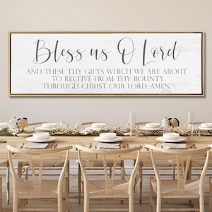 May include: A rectangular wall sign with a light wood frame featuring a white background and dark gray text that reads: Bless us O Lord and these thy gifts which we are about to receive from thy bounty through Christ our Lord. Amen.