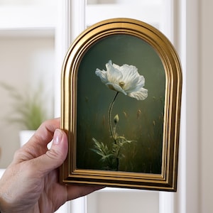 May include: A framed painting of a white poppy flower with a gold-colored frame. The artwork features a detailed depiction of the flower against a green and brown background. The frame has an arched top.