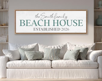 Puede incluir: Un letrero de pared rectangular horizontal con un marco de madera clara. El fondo blanco presenta el texto "the Smith family" en una fuente cursiva oscura, "BEACH HOUSE" en letras mayúsculas grandes de color verde azulado y "ESTABLISHED 2026" en letras mayúsculas oscuras.