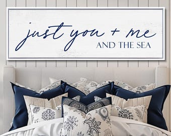 May include: A rectangular wall sign with a white wood-grain background and a dark blue frame. The text "just you + me AND THE SEA" is printed in dark blue, featuring a mix of cursive script for the first line and block lettering for the second.