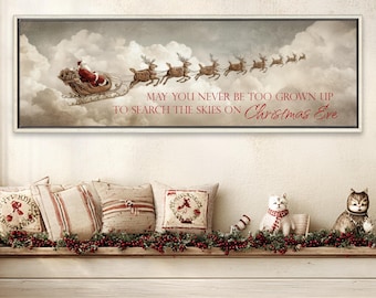 May include: A rectangular framed wall art print featuring a vintage-style illustration of Santa Claus in a sleigh pulled by reindeer flying through clouds. The text reads: MAY YOU NEVER BE TOO GROWN UP TO SEARCH THE SKIES ON Christmas Eve.