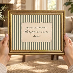 May include: A rectangular gold-toned picture frame containing a cream-colored background with vertical dark gray stripes. Centered in the frame is a piece of textured, deckled-edge paper with the text, your custom scripture verse here.
