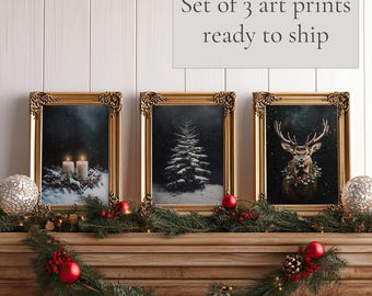 May include: Set of three gold framed art prints with winter scenes. The prints feature a snowy forest with candles, a snow-covered pine tree, and a deer with a wreath of holly around its neck. The prints are ready to ship.