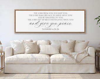 May include: A rectangular wall sign with a light wood frame featuring white background and dark gray text that reads: THE LORD BLESS YOU AND KEEP YOU; THE LORD MAKE HIS FACE TO SHINE UPON YOU AND BE GRACIOUS TO YOU; THE LORD LIFT UP HIS COUNTENANCE UPON YOU and give you peace NUMBERS 6:24-26.