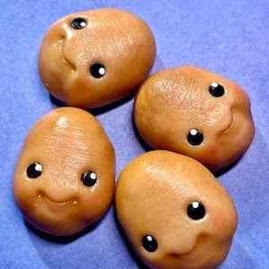 May include: Four small, tan-colored potato-shaped figurines with smiling faces and black eyes. The figurines are arranged on a blue surface. Each has a unique expression, adding to their charm.