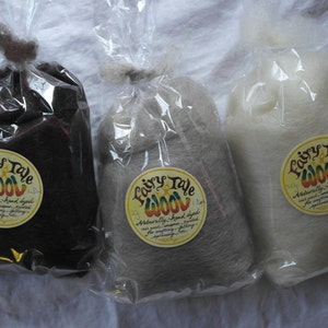Könnte beinhalten: Drei Beutel Fairy Tale Wool, eine natürlich handgefärbte Wolle zum Spinnen, Filzen und Nadelfilzen. Die Beutel sind mit dem Markennamen und einer Beschreibung der Wolle beschriftet. Die Wolle ist in drei Farben: Schwarz, Grau und Weiß.