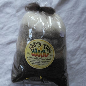 May include: A bag of Fairy Tale Wool, a naturally hand-dyed 100% wool fiber, in shades of brown, white, and gray. The bag is labeled with the brand name and details about the wool, including that it is 50g (1.8 oz).