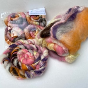 May include: A collection of hand-dyed wool roving in shades of pink, orange, purple, and brown. The roving is arranged in a variety of shapes and sizes, including a large, loose bundle and several smaller, tightly wound coils. The roving is perfect for spinning, felting, or other fiber crafts.