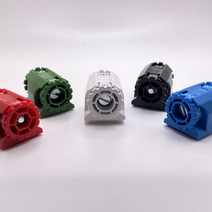 Puede incluir: Colección de dispositivos mecánicos multicolores y numerados. Los dispositivos son rojos, verdes, blancos, negros y azules. Cada uno tiene un dial circular con un número y un tornillo central. Dispuestos sobre una superficie blanca.