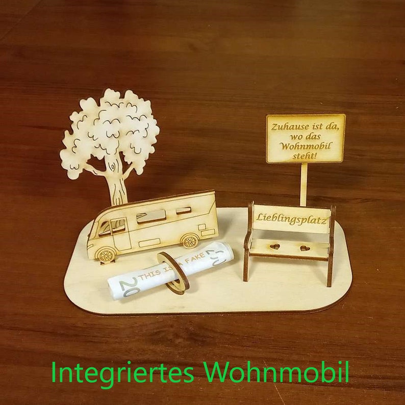 May include: A wooden model of a camper van with a tree, a bench, and a sign that reads "Zuhause ist da, wo das Wohnmobil steht!"  The model is on a wooden base with the words "Integriertes Wohnmobil" written on it.