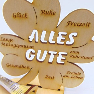 May include: A wooden clover-shaped sign with the words "ALLES GUTE" in white lettering. The sign has different phrases written on each leaf, including "Ruhe", "Freizeit", "Lange Mittagspausen", "Gesundheit", "Zeit", and "Freude am Leben".