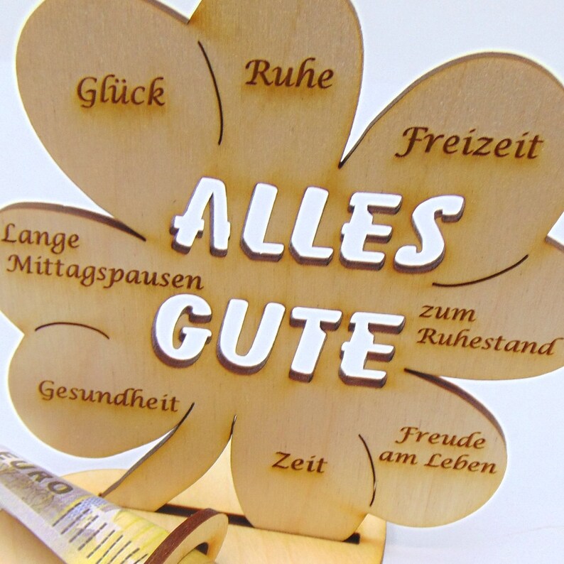 May include: A wooden clover-shaped sign with the words "ALLES GUTE" in white lettering. The sign has different phrases written on each leaf, including "Ruhe", "Freizeit", "Lange Mittagspausen", "Gesundheit", "Zeit", and "Freude am Leben".