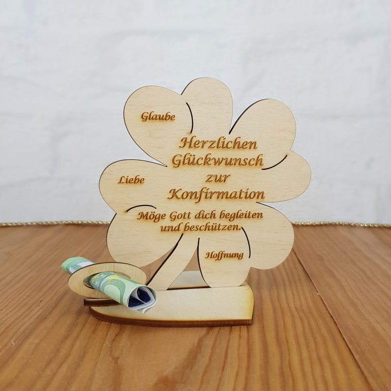 Op de afbeelding: Houten klavertje vier kaart met de tekst "Herzlichen Gl&uuml;ckwunsch zur Konfirmation" en "M&ouml;ge Gott dich begleiten und besch&uuml;tzen." De kaart heeft een gleuf voor geld of een cadeaubon.